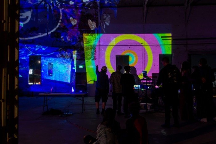 Silhouetted attendees in front of a giant concentric pink, yellow, and green spiral projection